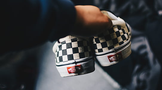 person holding white-and-black Vans slip-on shoes thumbnail