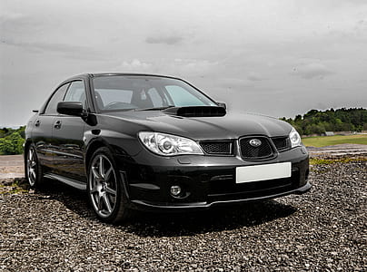 black Subaru Impreza parked on grey gravel under gray clouds thumbnail