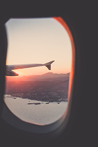 airplane wing through window overlooking island with body of water photography thumbnail