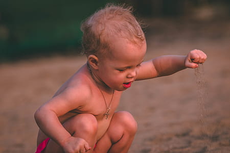 Baby With Pendant Necklace Holding Sand at Daytime thumbnail