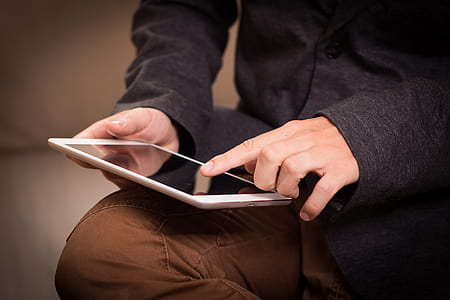 person wearing black dress shirt and brown pants holding white ipad thumbnail