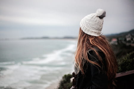 woman looking on open sea wearing white knit bobble cap thumbnail
