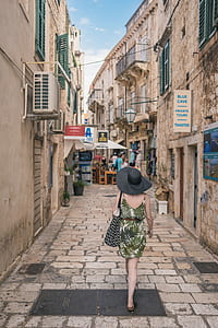photo of woman in green dress walking on pathway between houses thumbnail