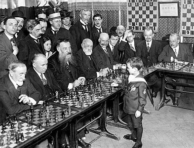 grayscale photo of group of men vs boy playing chess game thumbnail