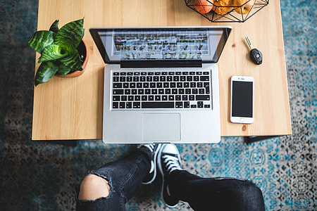 Woman in ripped jeans and black sneakers with a silver laptop on a wooden table thumbnail