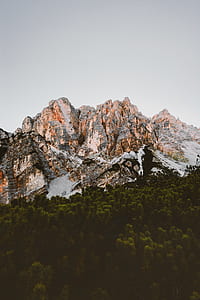 landscape photography of rocky mountain and green leaf trees under cloudy sky thumbnail