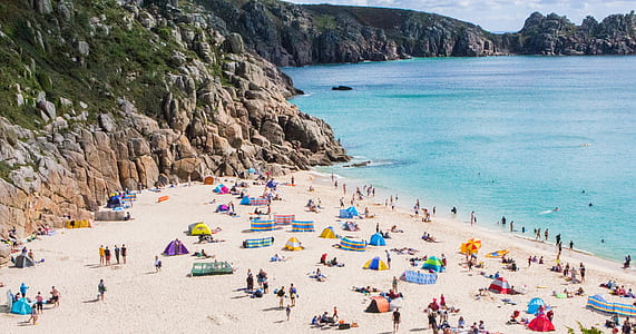 people sunbathing and standing on beach near mountains thumbnail