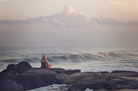 woman in dress sitting on rock near body of water thumbnail
