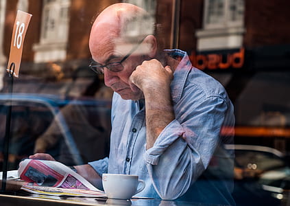 man reading magazine near glass windowpane thumbnail