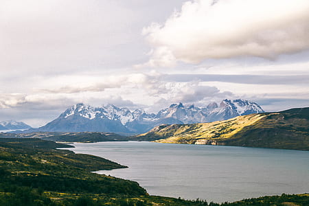 body of water between mountain under cloudy sky at daytime thumbnail