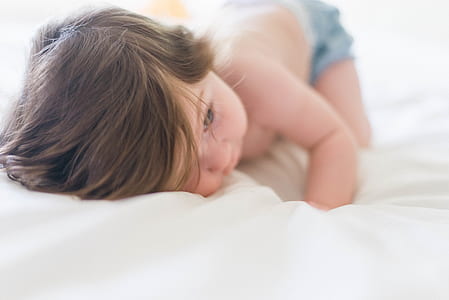 baby wearing blue bottoms lying on white cushion thumbnail