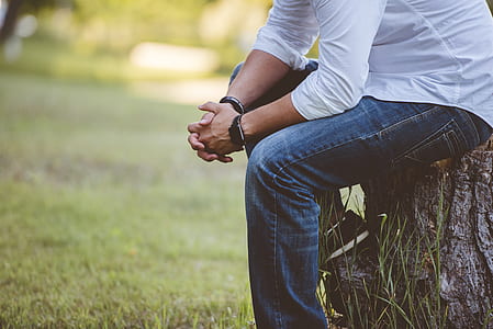 selective focus photography of person wearing white dress shirt and blue denim jeans sitting on brown stump over green grass thumbnail