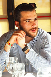 man sitting beside table looking at his left thumbnail