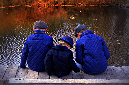 three boys sitting on boardwalk during daytime thumbnail