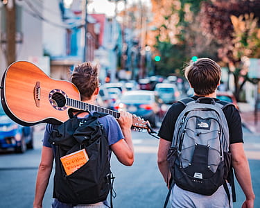 two man walking on street with backpack and holding guitar thumbnail