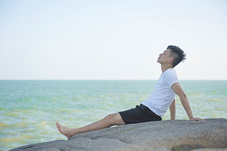 man resting on rock formation near body of water thumbnail
