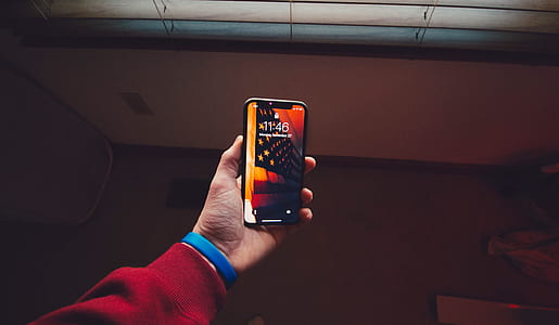 person holding space gray iPhone X displaying lock screen thumbnail