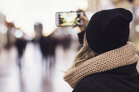 woman in black coat and brown knitted scarf holding white smartphone thumbnail