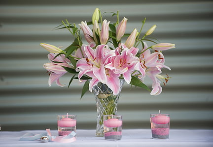 pink petaled flowers in clear vase beside three candle holders thumbnail