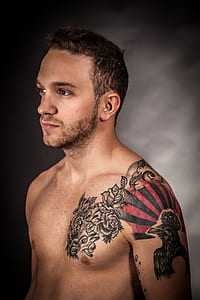 topless man standing with eagle and flower arm tattoos thumbnail