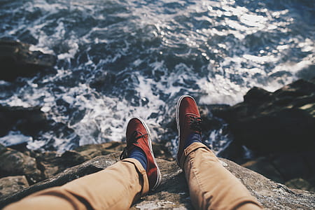 person wearing red lace up shoes sitting on rock near body of water during daytime thumbnail