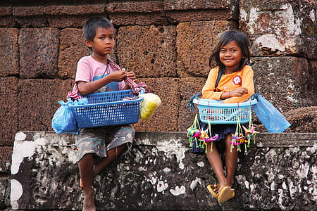 two boy and girl sitting on a concrete wall while carrying basket of goods thumbnail