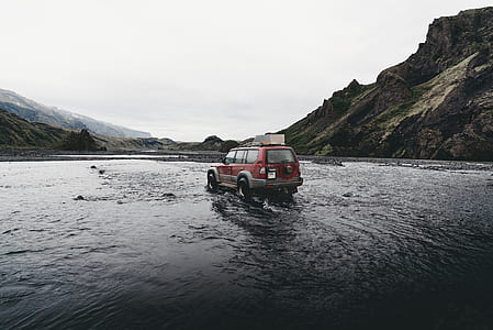 red SUV running at rive beside mountain thumbnail