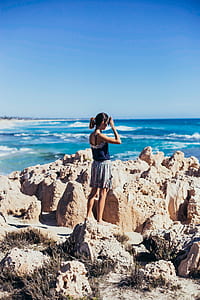 woman standing on edge of cliff facing ocean during daytime thumbnail