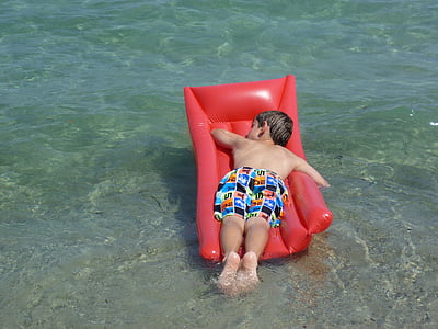 boy lying on red floater during daytime thumbnail