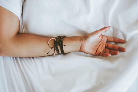 person wearing black and gray bracelet lying on white textile thumbnail