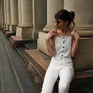 woman wearing white dungaree pants sitting near concrete pillar at daytime thumbnail