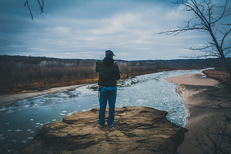 man in blue denim pants standing on brown rock looking at the river thumbnail
