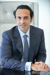 man wearing dark-blue suit sitting down on white leather chair thumbnail