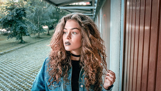 woman wearing blue denim jacket holding her curly hair thumbnail