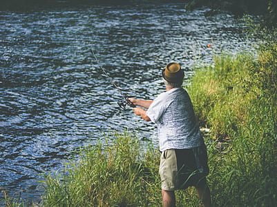 person in white tank holding fishing rod in front of body of water during daytime thumbnail