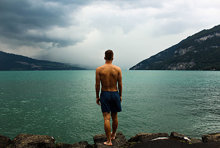 man in black short standing on rock beside lake thumbnail