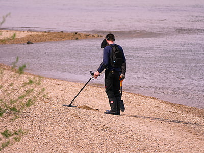 man using metal detector and holding shovel walking on beach thumbnail