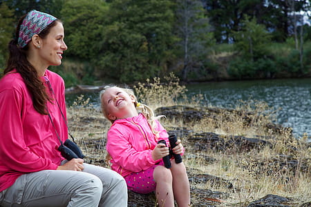 woman and girl holding binocular sitting on stones thumbnail