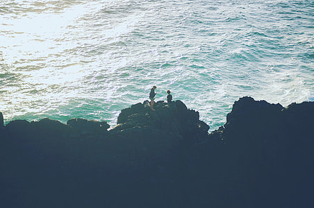bird's-eye view photography of two person standing on top of mountain near body of water thumbnail