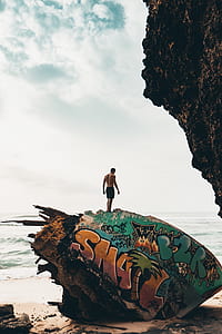 man wearing black shorts standing on big rock near body of water under white sky during daytime thumbnail