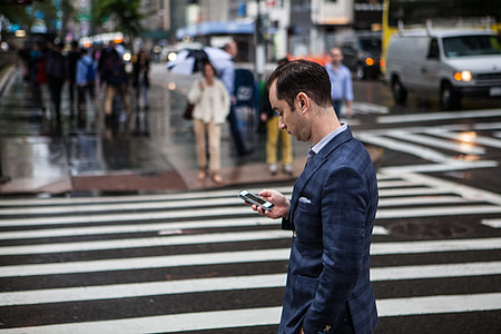 A man checks his mobile iPhone smartphone on a rainy day on the streets of Manhattan, New York City thumbnail