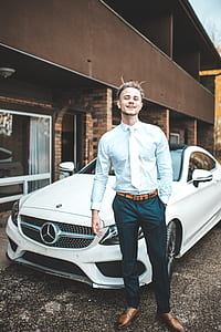 man wearing teal dress shirt, white necktie and green pants standing near white Mercedes-Benz coupe thumbnail