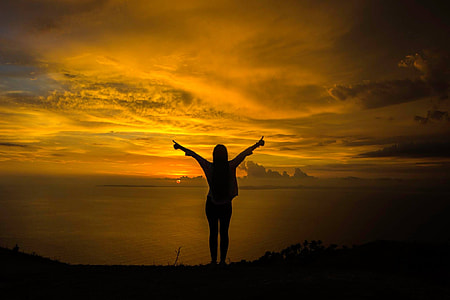 silhouette photo of woman standing on cliff facing ocean during sunset thumbnail