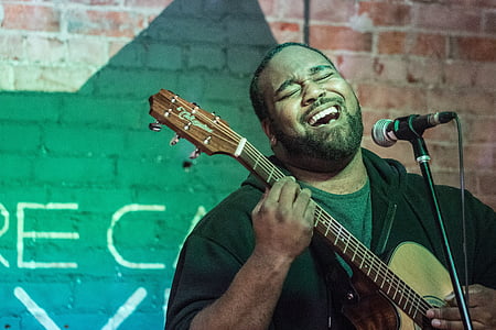 man singing on black microphone while playing brown acoustic guitar thumbnail