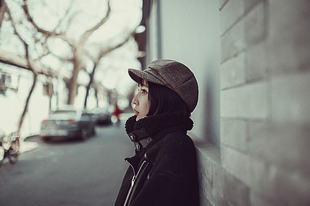 woman in black zip-up jacket leaning on wall during daytime thumbnail