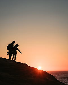 silhouette of man and woman on top of mountain cliff during sunset thumbnail