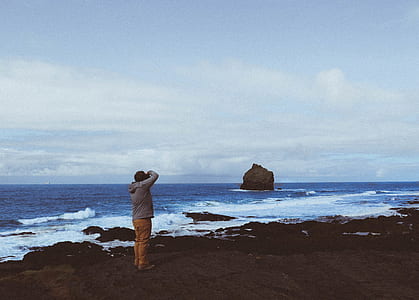 man standing on seashore capturing rock thumbnail