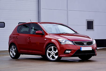 red Kia 5-door hatchback parked near white walled building thumbnail