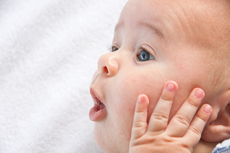 baby holding face laying on white textile thumbnail