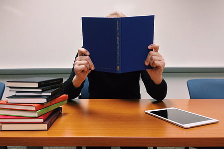person holding blue book sitting infront of brown wooden table thumbnail